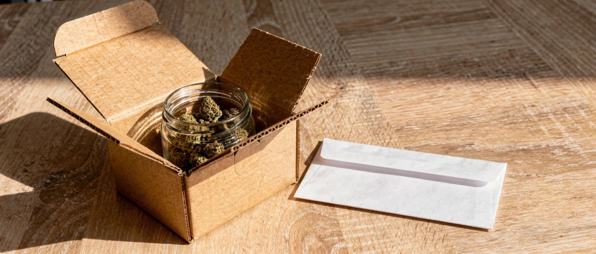 Offenes Versandpaket mit Glas voller Hanfblüten und Briefumschlag auf Holz, Thema Bestellung auf Rechnung