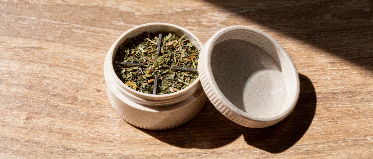 Geöffneter Kräutergrinder mit gemahlener Hanfblüte auf hellem Eichenholz, Thema Purize Grinder